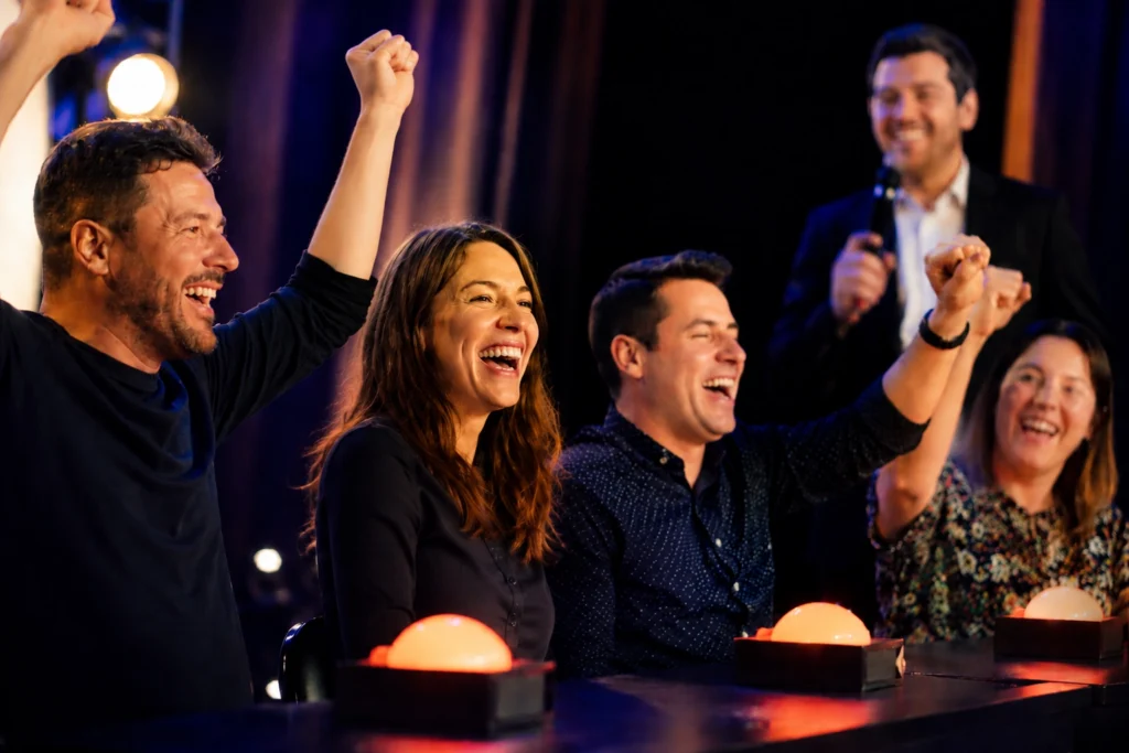 Amis célébrant leur victoire lors d'une sortie entre amis à Showtime Quiz Vitrolles, buzzers lumineux et animateur en arrière-plan